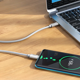 Smartphone charging via cable connected to a laptop on a wooden surface