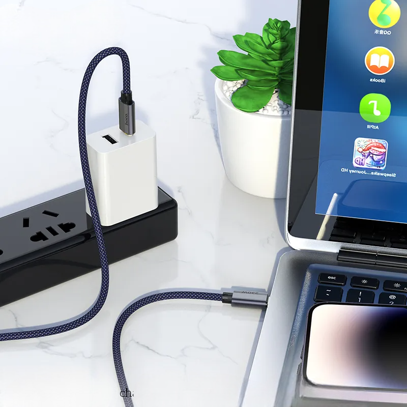 Laptop with USB-C hub and cable on a white surface with a plant in the background