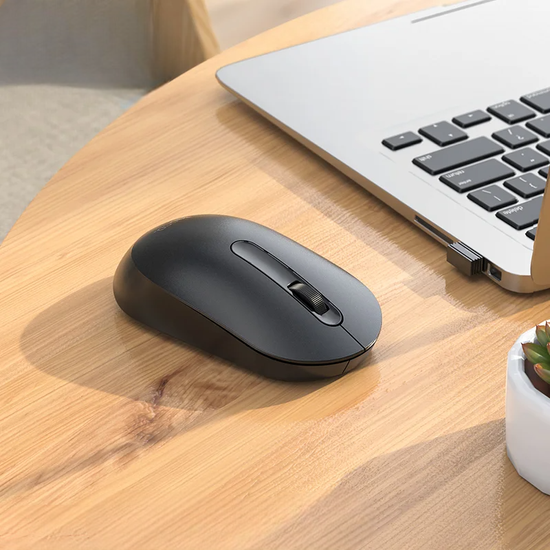 Black wireless mouse on a wooden desk next to a laptop