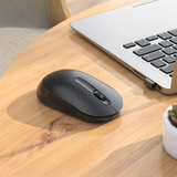 Black wireless mouse on a wooden desk next to a laptop