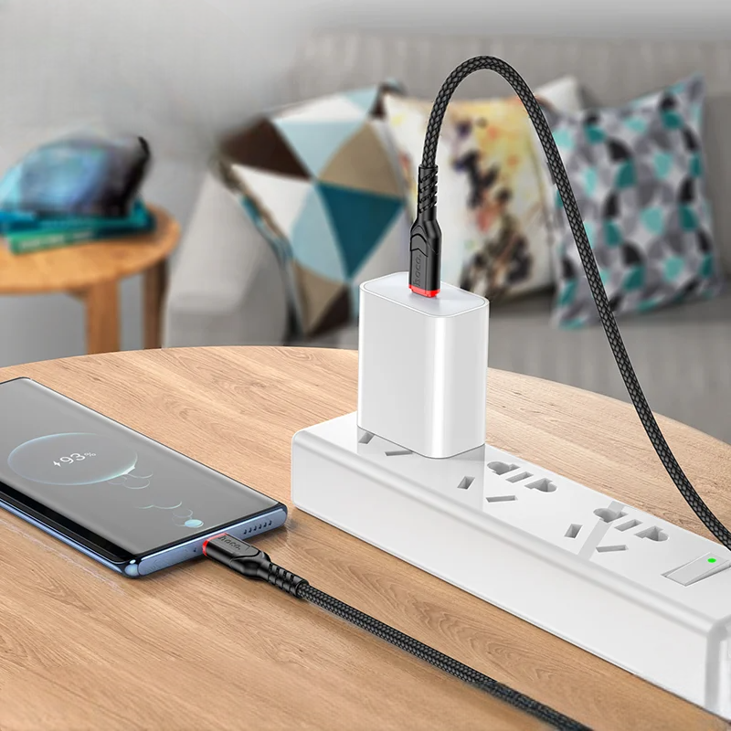 White power strip with multiple outlets on a wooden surface, with a smartphone charging cable plugged into one of the outlets.