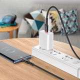 White power strip with multiple outlets on a wooden surface, with a smartphone charging cable plugged into one of the outlets.