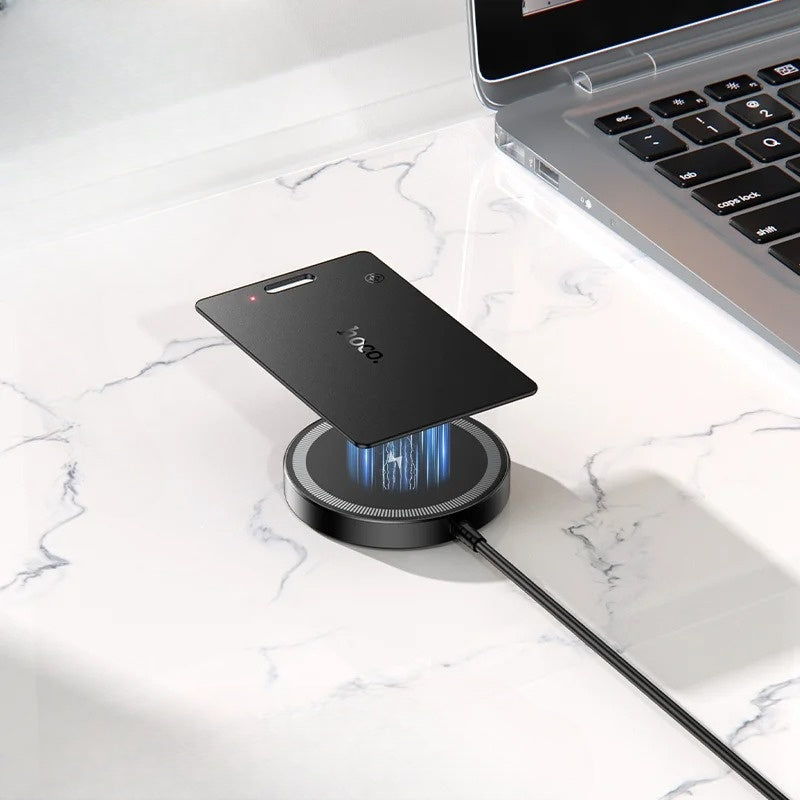 Black smartphone on a wireless charging pad with a laptop in the background on a marble surface