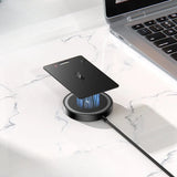 Black smartphone on a wireless charging pad with a laptop in the background on a marble surface