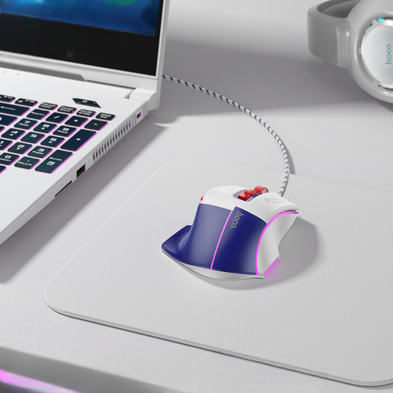 Gaming mouse on a desk with a laptop and headphones in the background