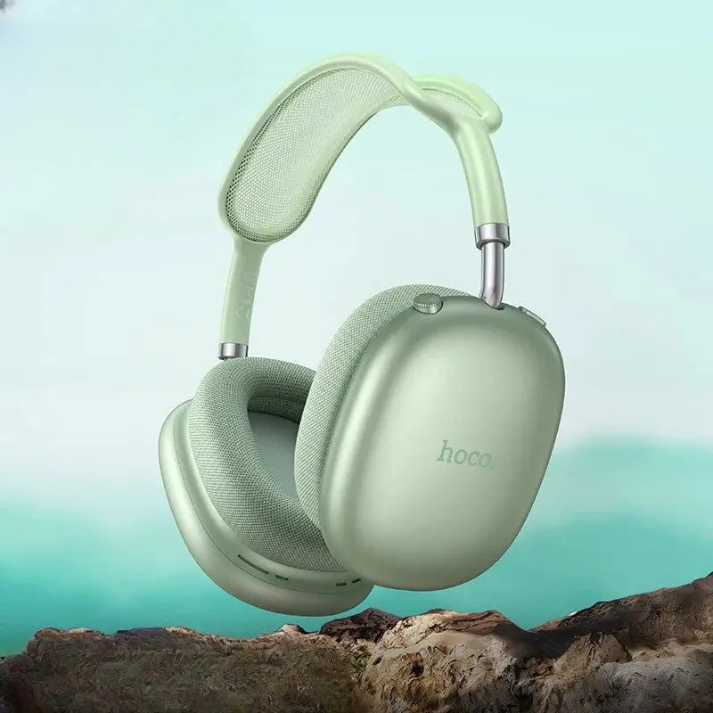 Light green headphones with 'hoco' branding on a blurred natural background