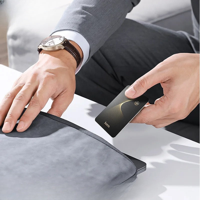 Person holding a black phone with 'hoco' branding on a light gray surface.