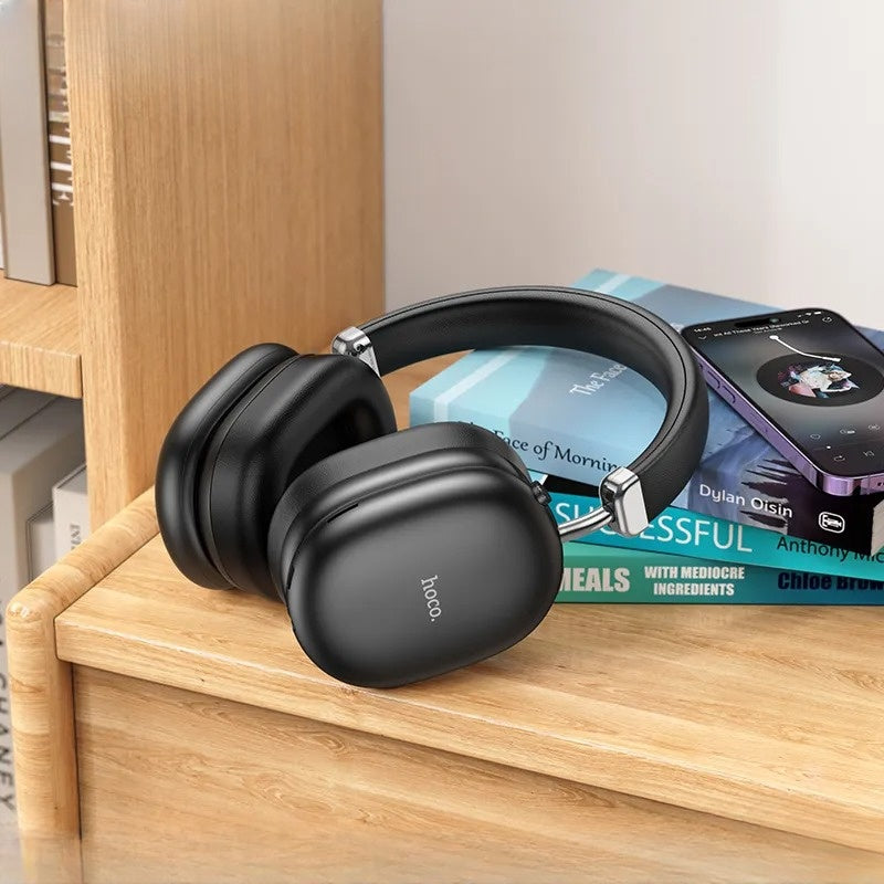 Black headphones on a wooden surface with books and a phone in the background