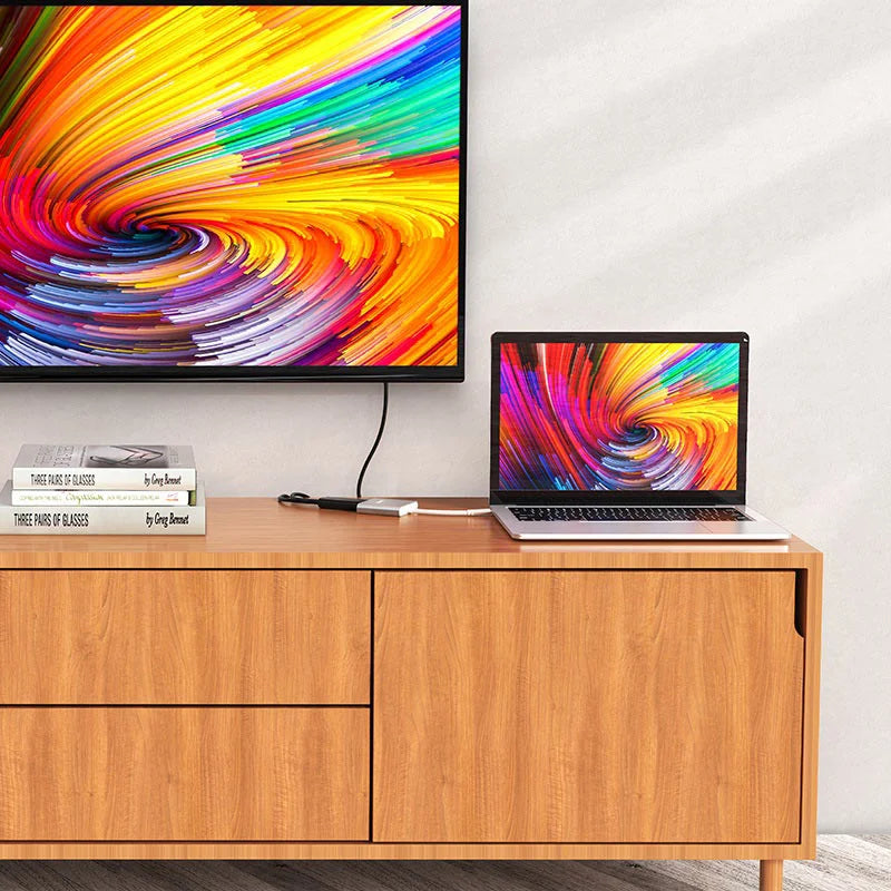 Laptop and TV displaying colorful abstract patterns on a wooden cabinet.